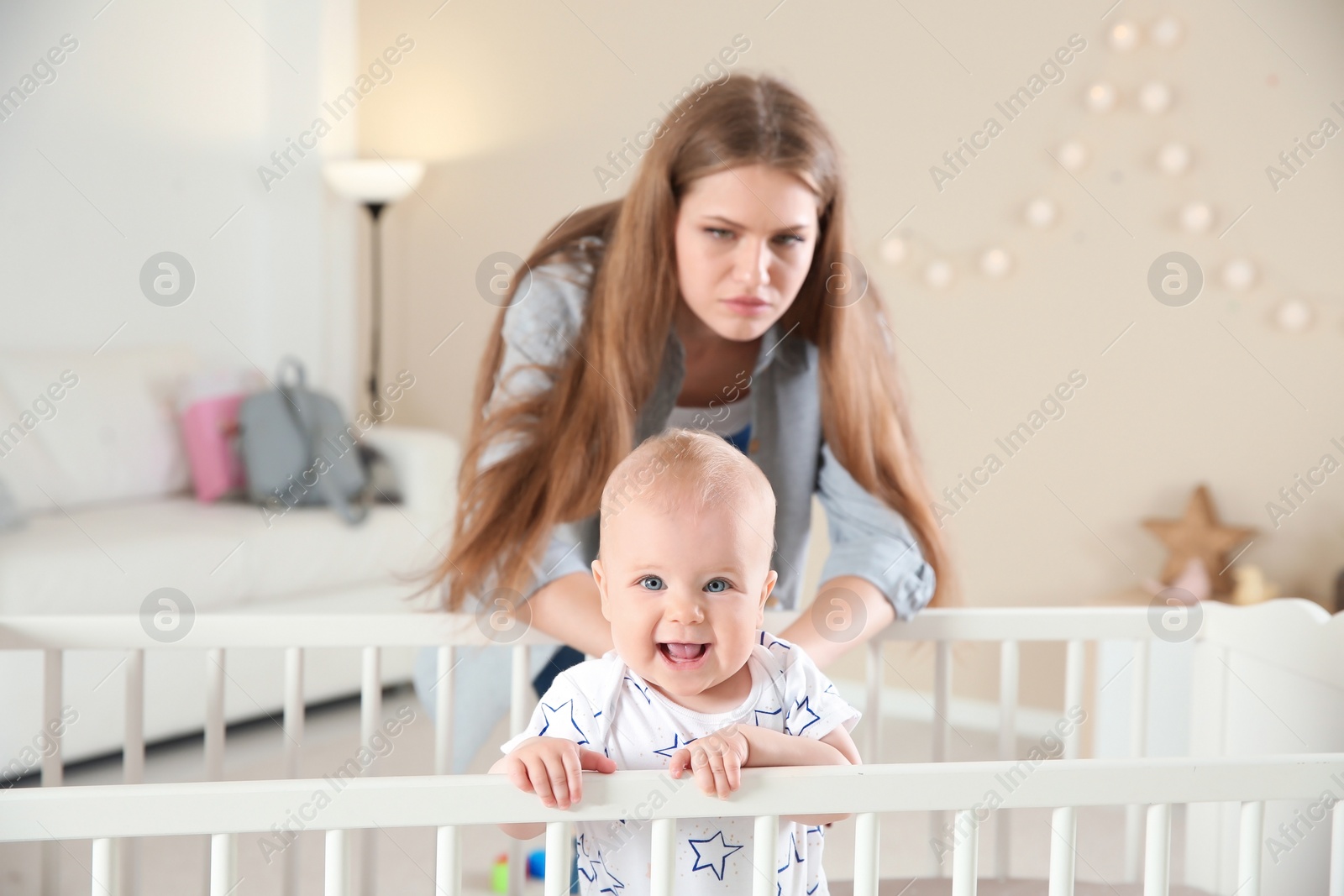 Photo of Cute baby girl in crib and young mother suffering from postnatal depression at home