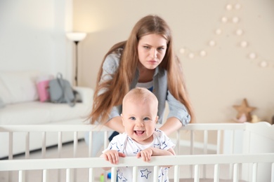 Photo of Cute baby girl in crib and young mother suffering from postnatal depression at home