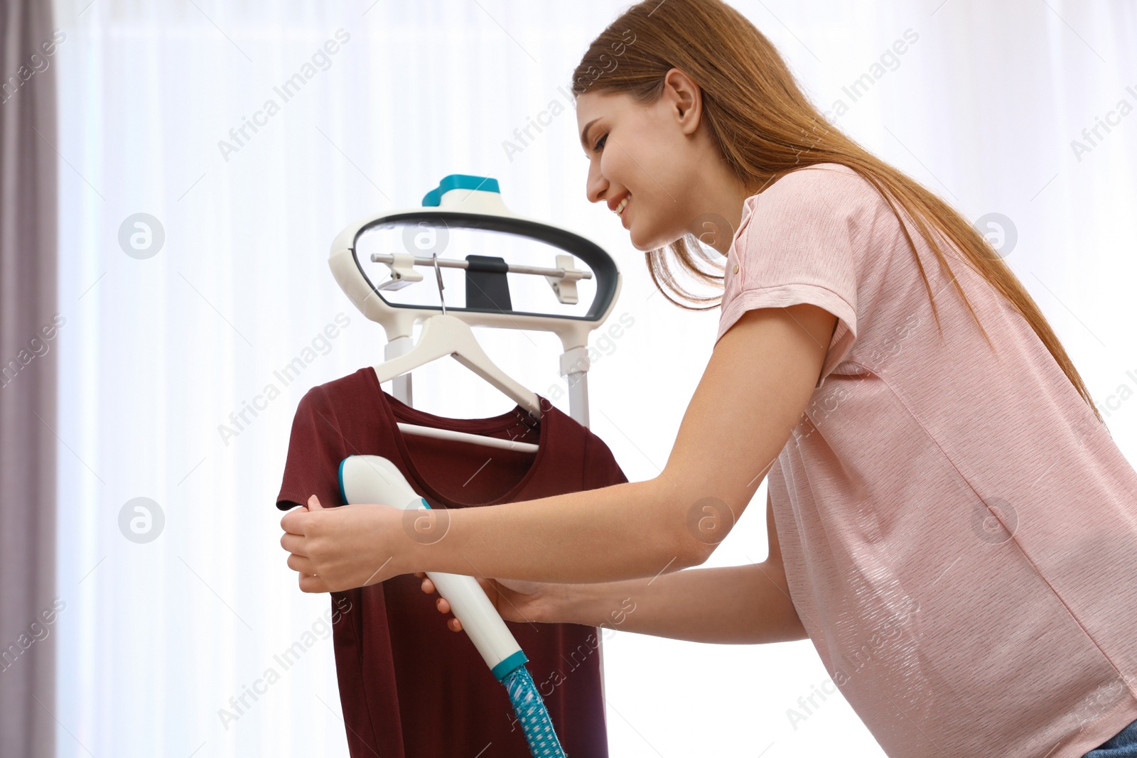 Photo of Young woman steaming her clothes on rack at home