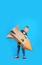 Photo of Little child playing with rocket made of cardboard box on light blue background. Space for text