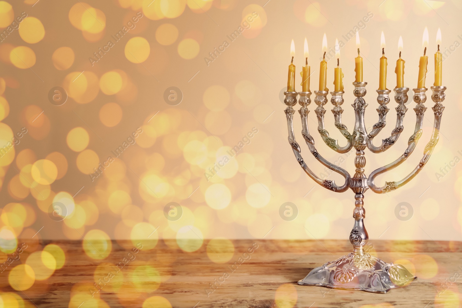 Image of Silver menorah with burning candles on wooden table against beige background, space for text. Hanukkah celebration