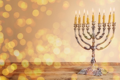 Image of Silver menorah with burning candles on wooden table against beige background, space for text. Hanukkah celebration