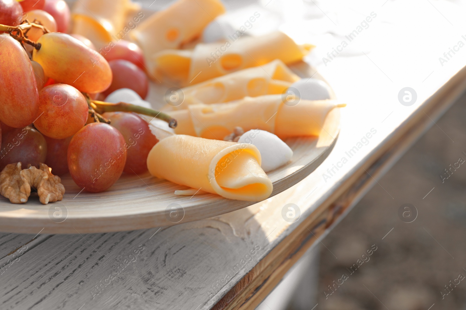 Photo of Plate with cheese and grapes on white wooden table outdoors, closeup view