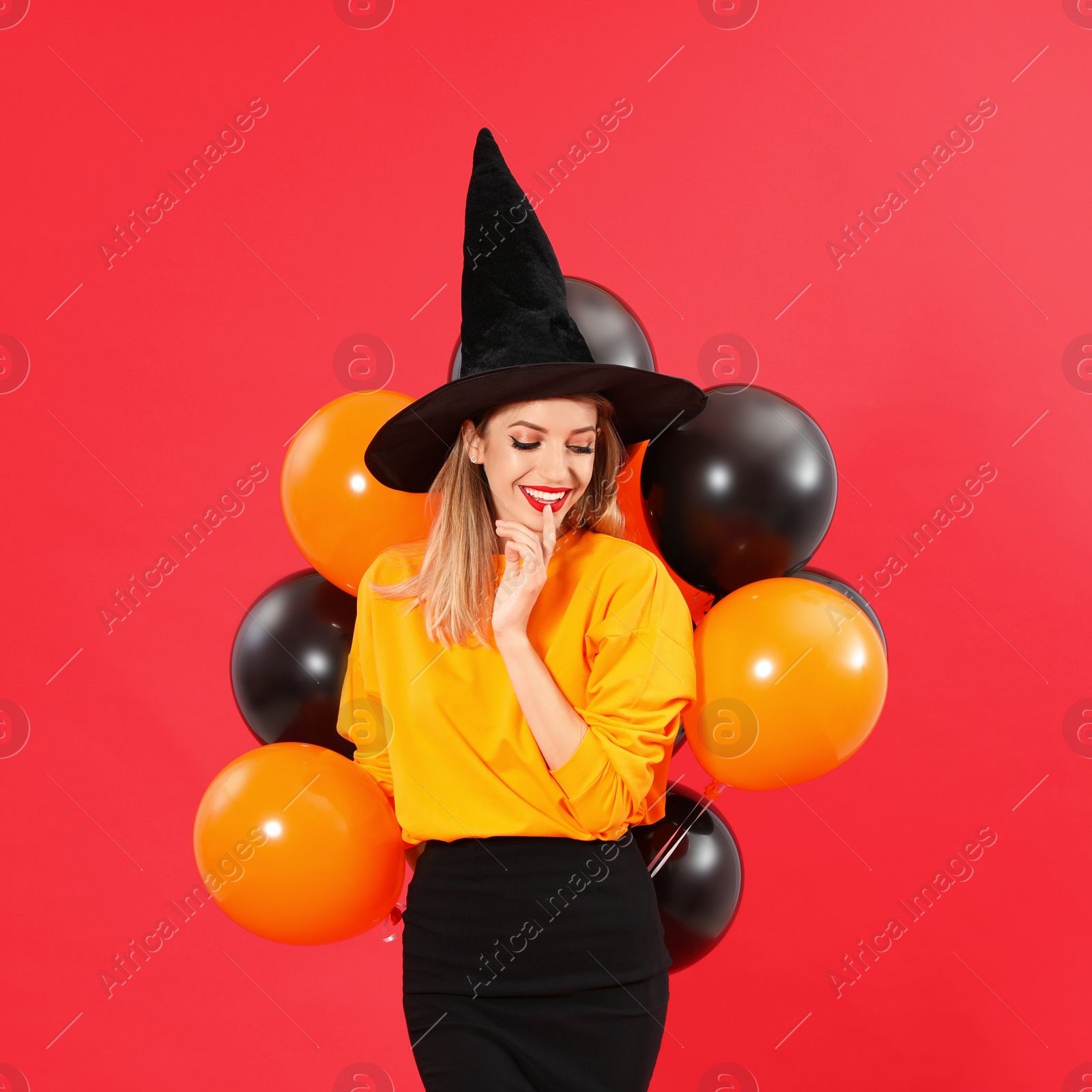 Photo of Beautiful woman wearing witch costume with balloons for Halloween party on red background