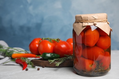 Photo of Jar with pickled tomatoes and vegetables on grey table against blue background