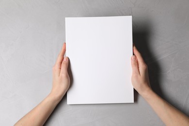 Woman holding notebook with blank cover at light grey table, top view. Mockup for design