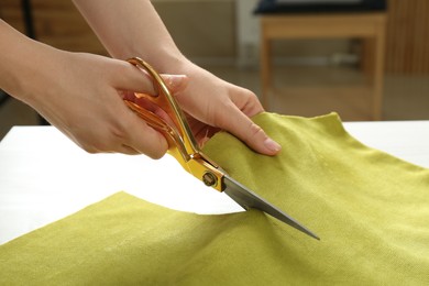Photo of Seamstress cutting light green fabric with scissors at workplace, closeup