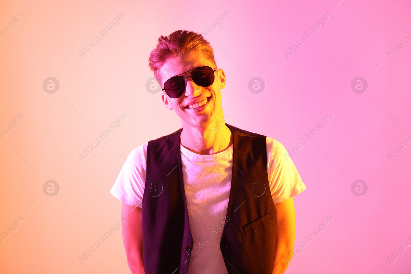 Photo of Stylish young man in sunglasses on pink background in neon lights