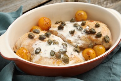 Delicious chicken fillets with capers, tomatoes and sauce in baking dish on table, closeup