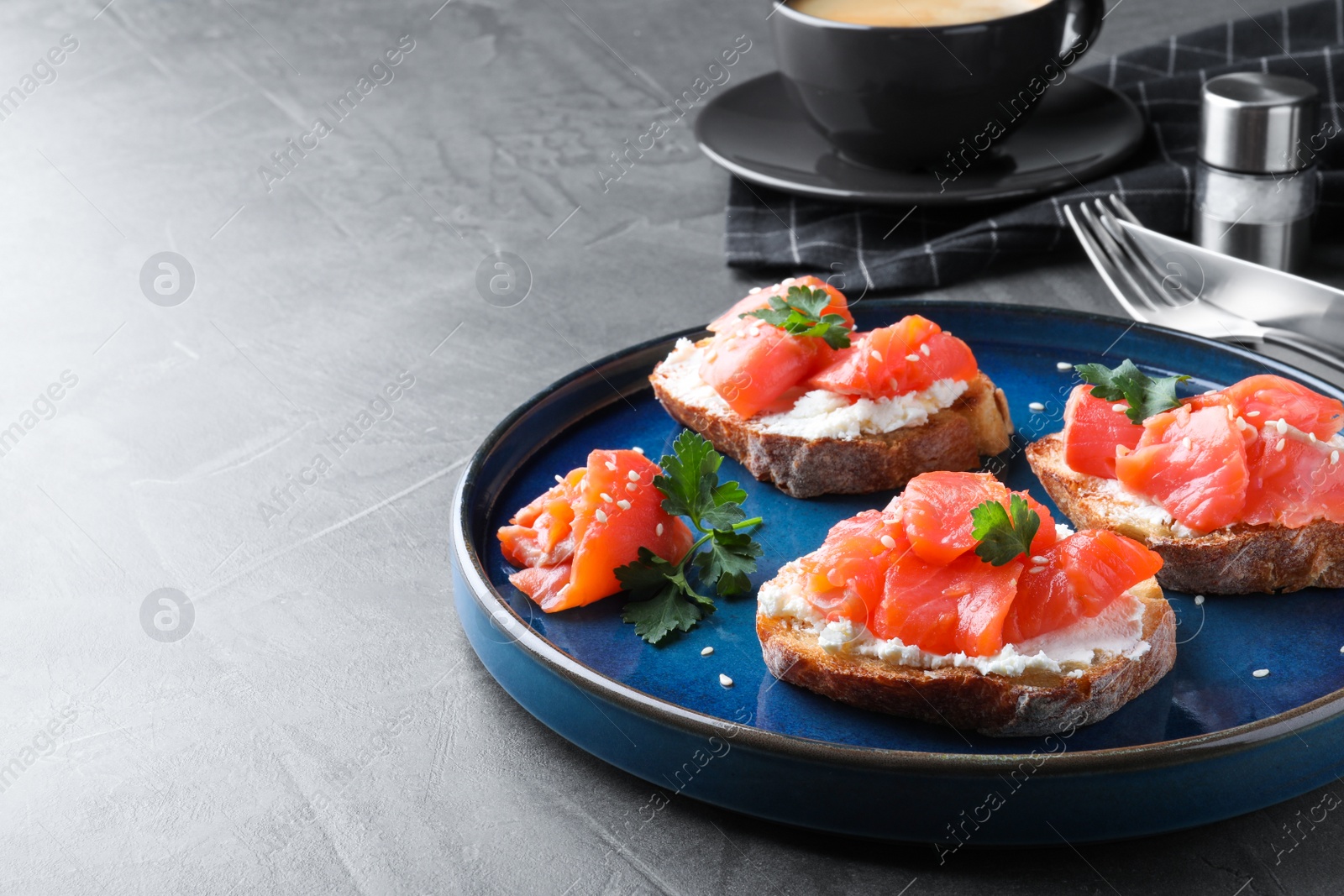 Photo of Tasty bruschettas with salmon, cream cheese and parsley on grey table, space for text