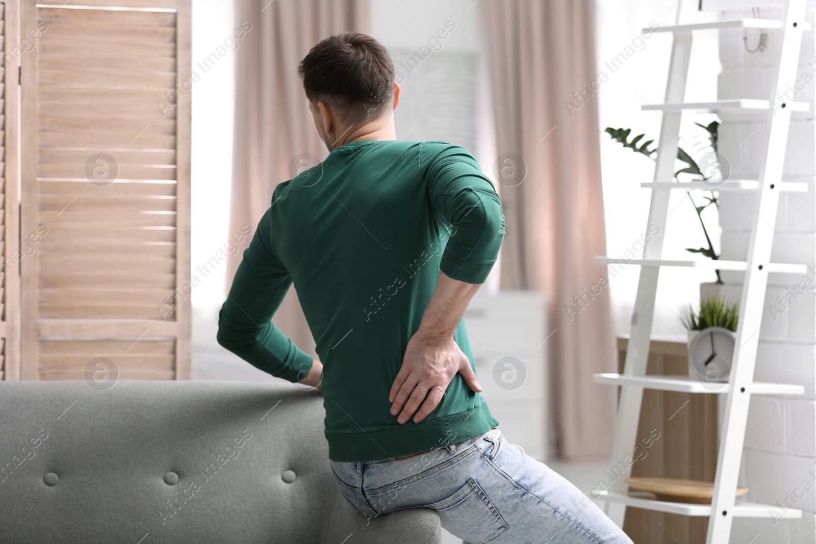 Photo of Young man suffering from back pain at home