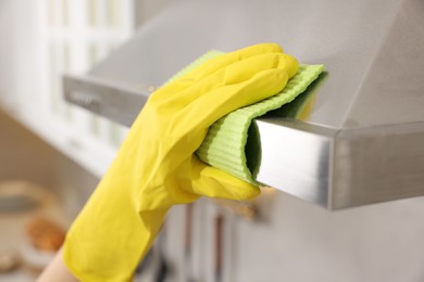 Photo of Woman with spray bottle and microfiber cloth cleaning kitchen hood indoors, closeup