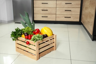 Photo of Wooden crate with vegetables on floor in kitchen. Space for text