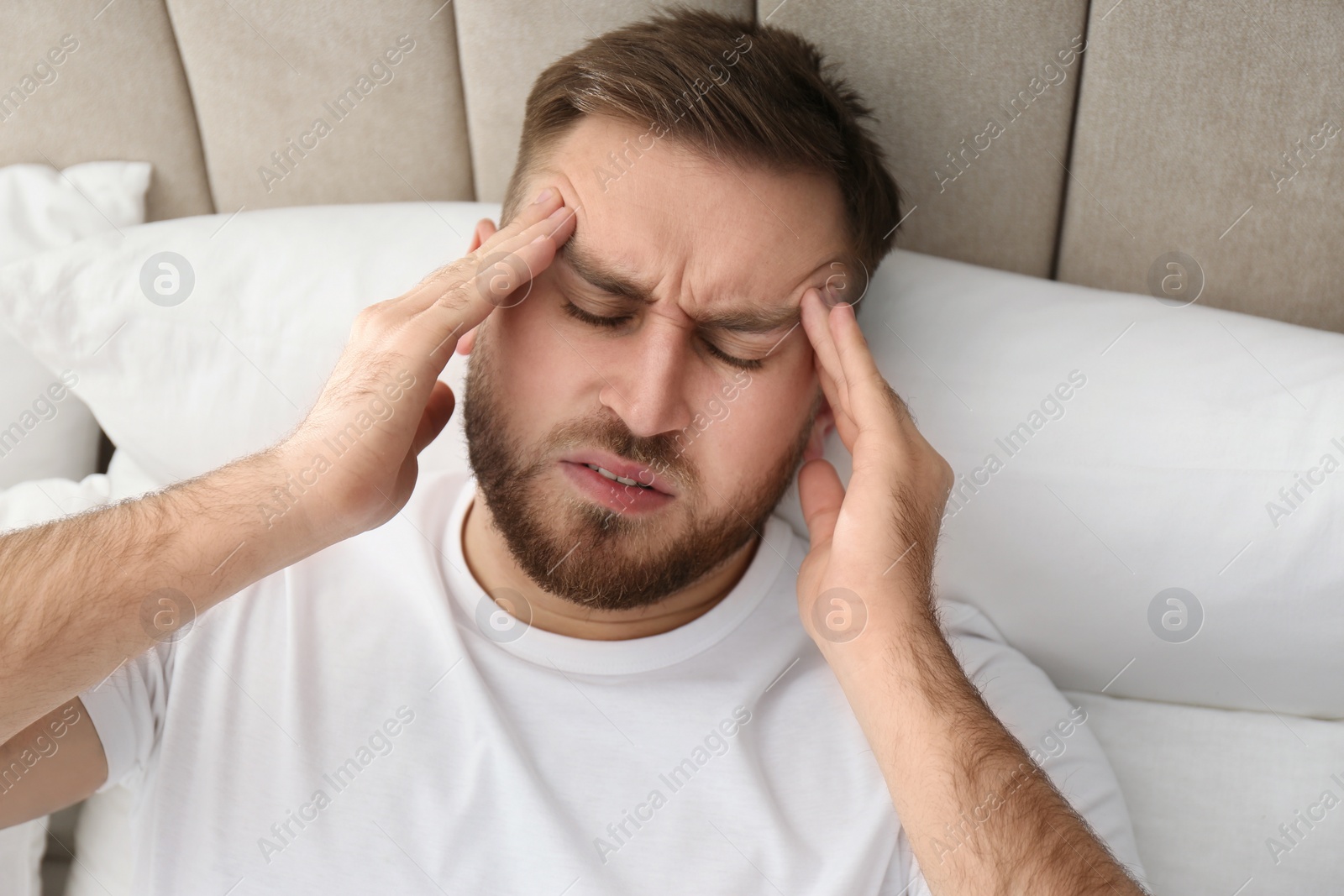 Photo of Young man suffering from migraine in bed, above view