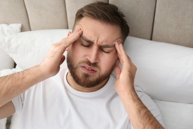 Photo of Young man suffering from migraine in bed, above view