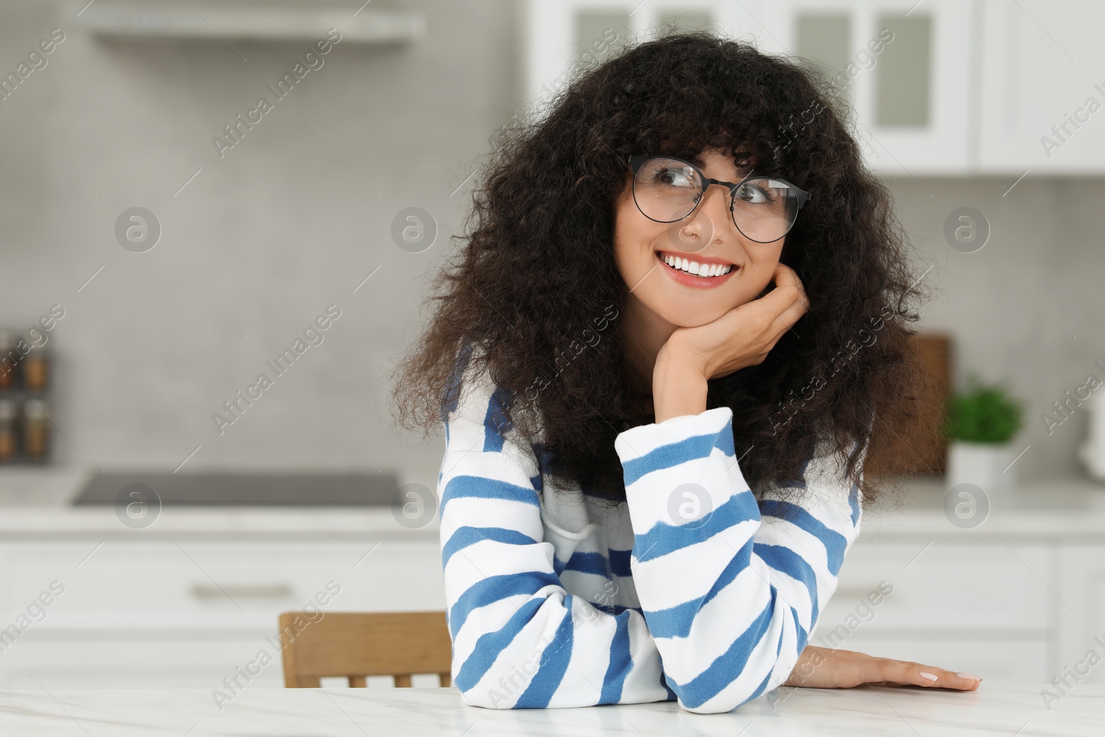 Photo of Portrait of beautiful woman with curly hair in kitchen. Attractive lady smiling and posing for camera. Space for text