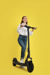Happy woman with modern electric kick scooter on yellow background