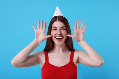 Happy woman in party hat on light blue background