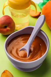Photo of Healthy baby food in bowl on light green background