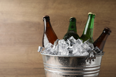 Photo of Metal bucket with beer and ice cubes on wooden background. Space for text