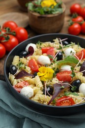 Photo of Bowl of delicious pasta with tomatoes, olives and mozzarella on wooden table, closeup