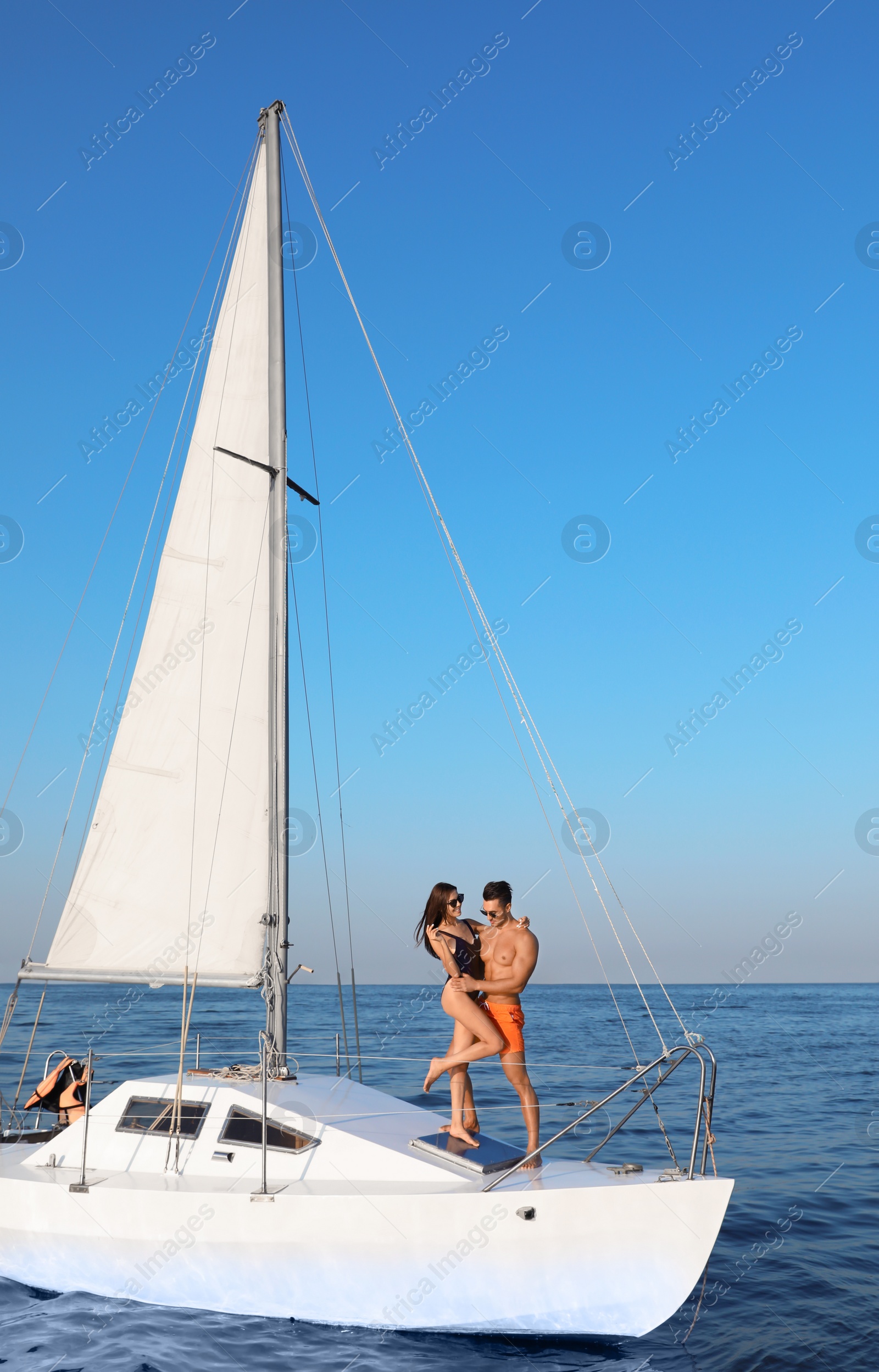 Photo of Young man and his beautiful girlfriend in bikini on yacht. Happy couple during sea trip