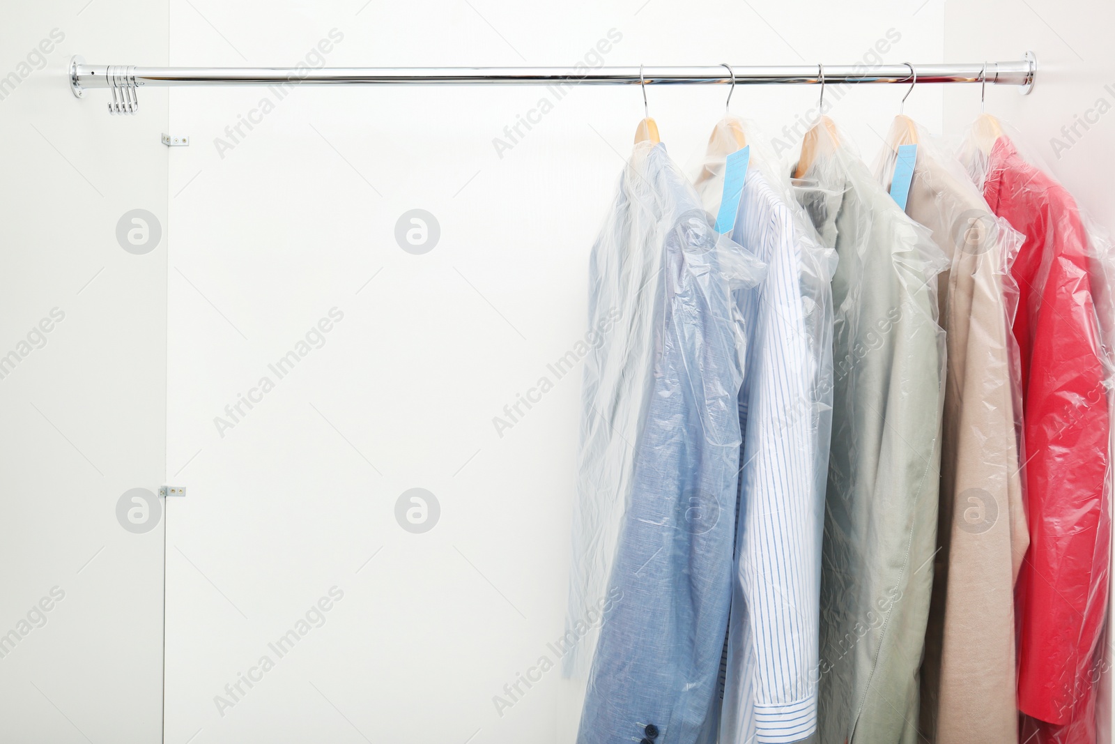 Photo of Rack with clean clothes after dry-cleaning on hangers in wardrobe