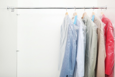 Photo of Rack with clean clothes after dry-cleaning on hangers in wardrobe