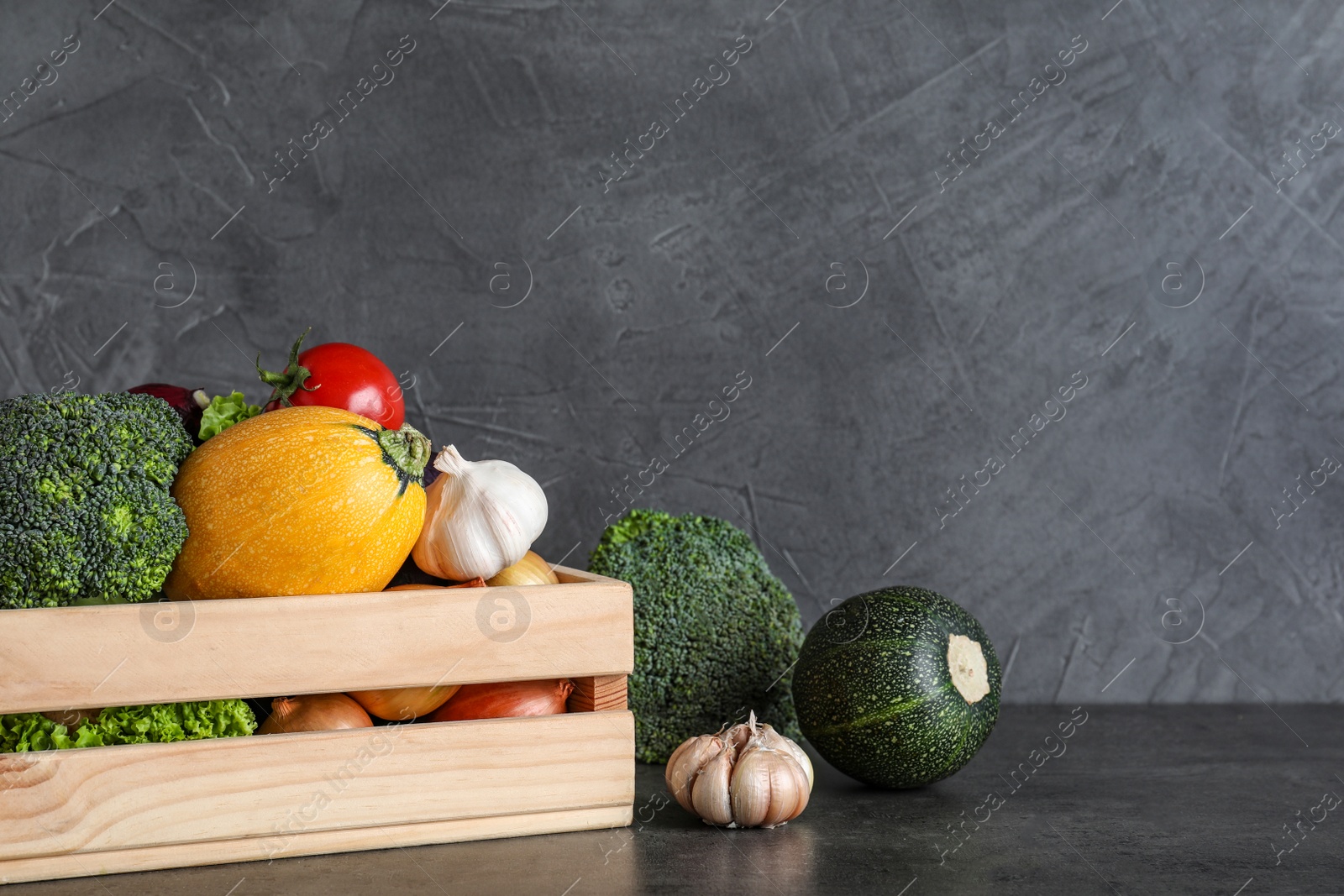 Photo of Wooden crate filled with delicious fresh vegetables on table against color background, space for text