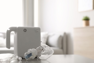 Photo of Modern nebulizer with face mask on white table indoors, space for text. Inhalation equipment