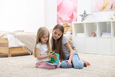 Photo of Cute little sisters reading book together at home