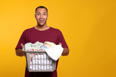 Emotional man with basket full of laundry on orange background