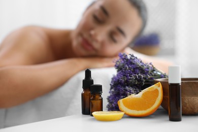 Woman relaxing on massage couch and bottles of essential oil with ingredients on table in spa salon, selective focus