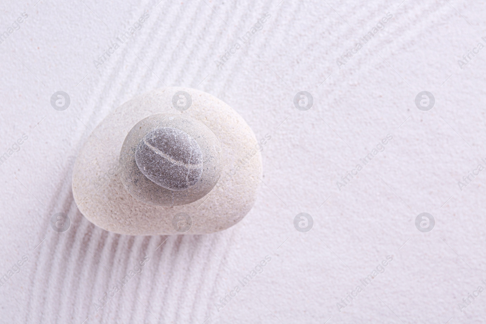 Photo of Zen garden stones on white sand with pattern, top view. Space for text