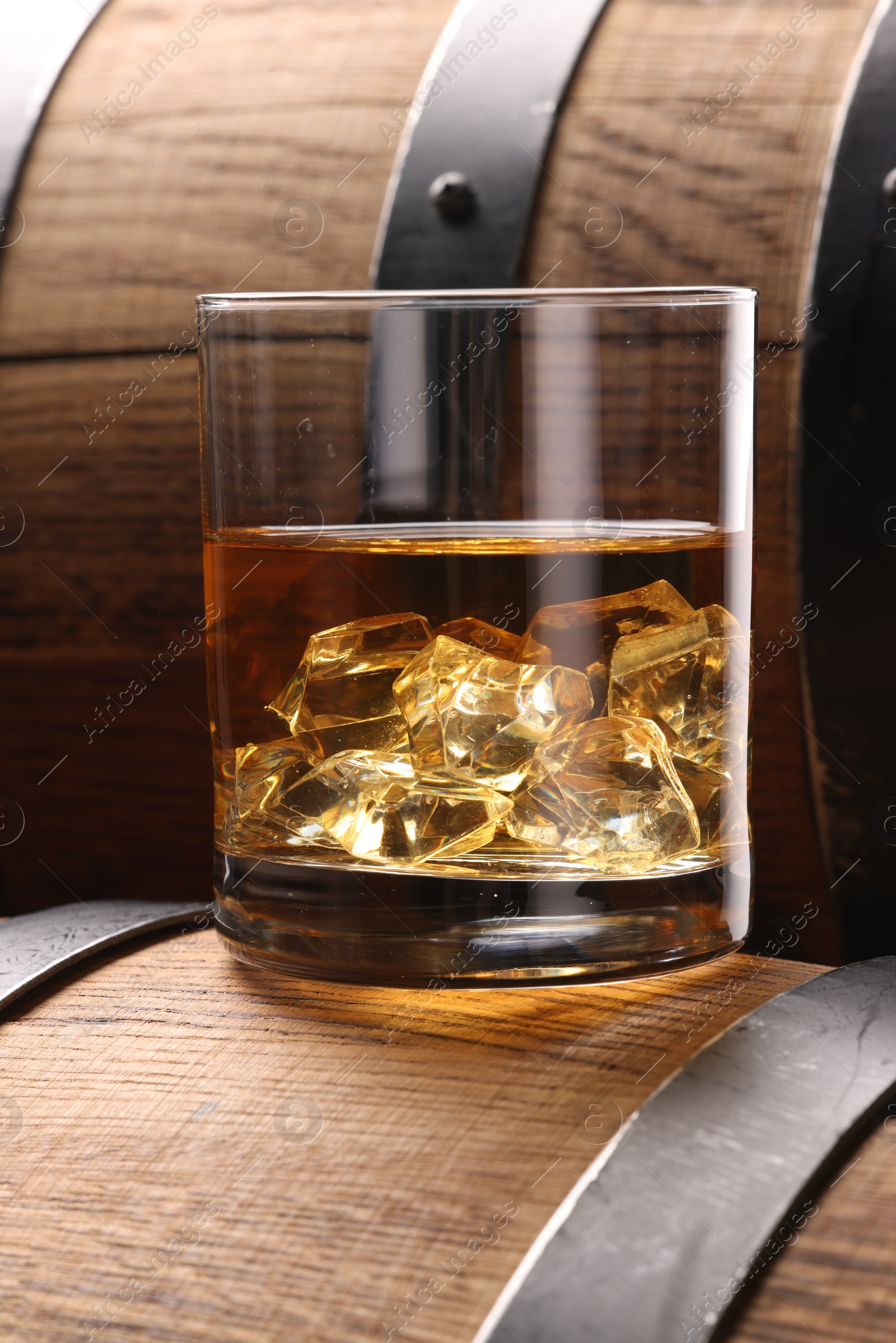Photo of Whiskey with ice cubes in glass on wooden barrel, closeup