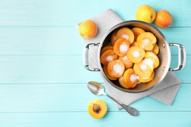 Pot with apricots and sugar on light blue wooden table, space for text. Making delicious jam