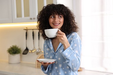 Photo of Beautiful young woman in stylish pyjama with cup of drink in kitchen