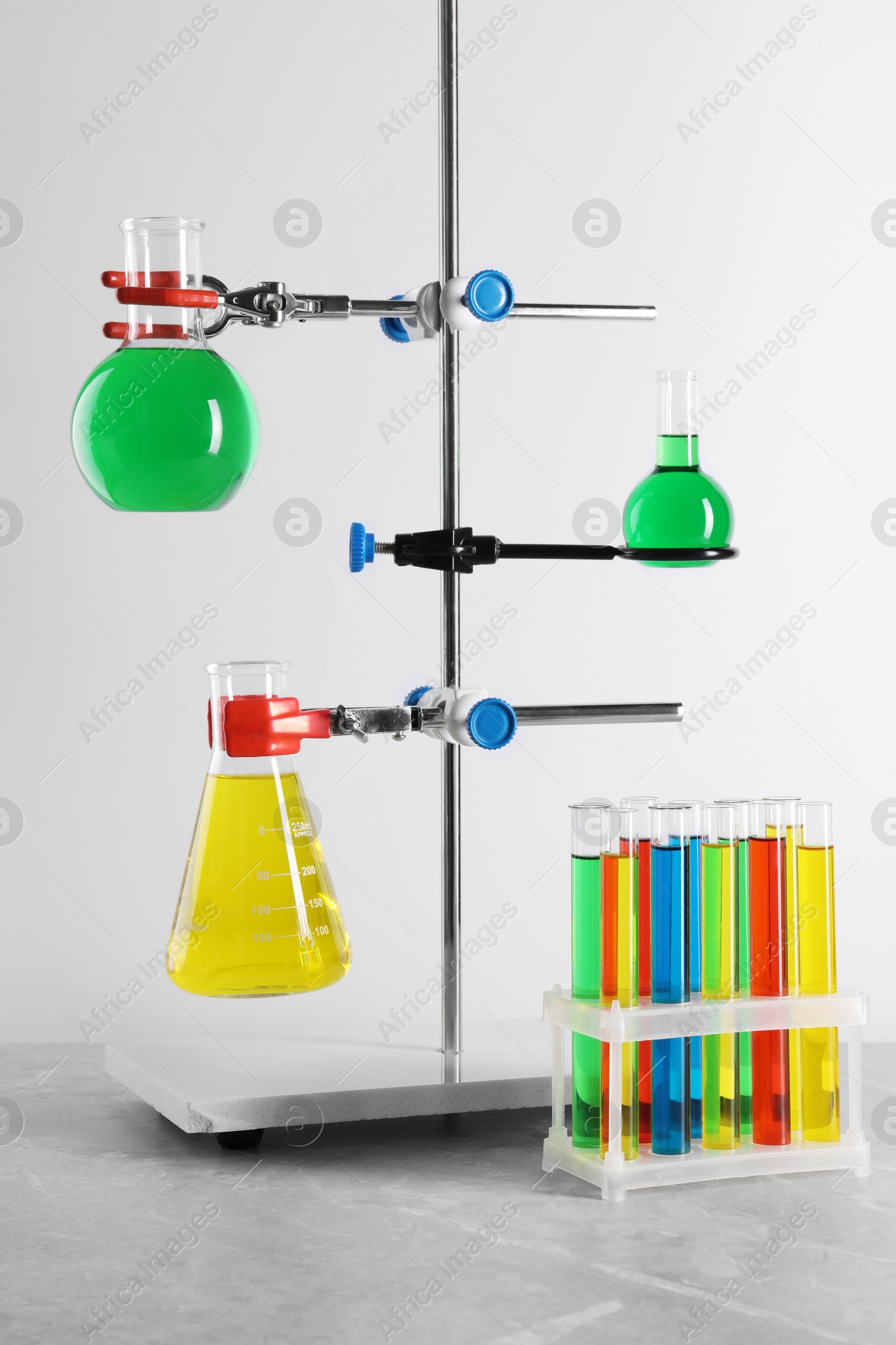 Photo of Retort stand and laboratory glassware with liquids on grey table against white background