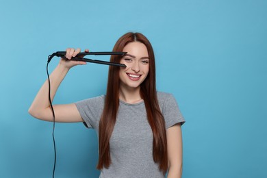 Photo of Beautiful woman with hair iron on light blue background