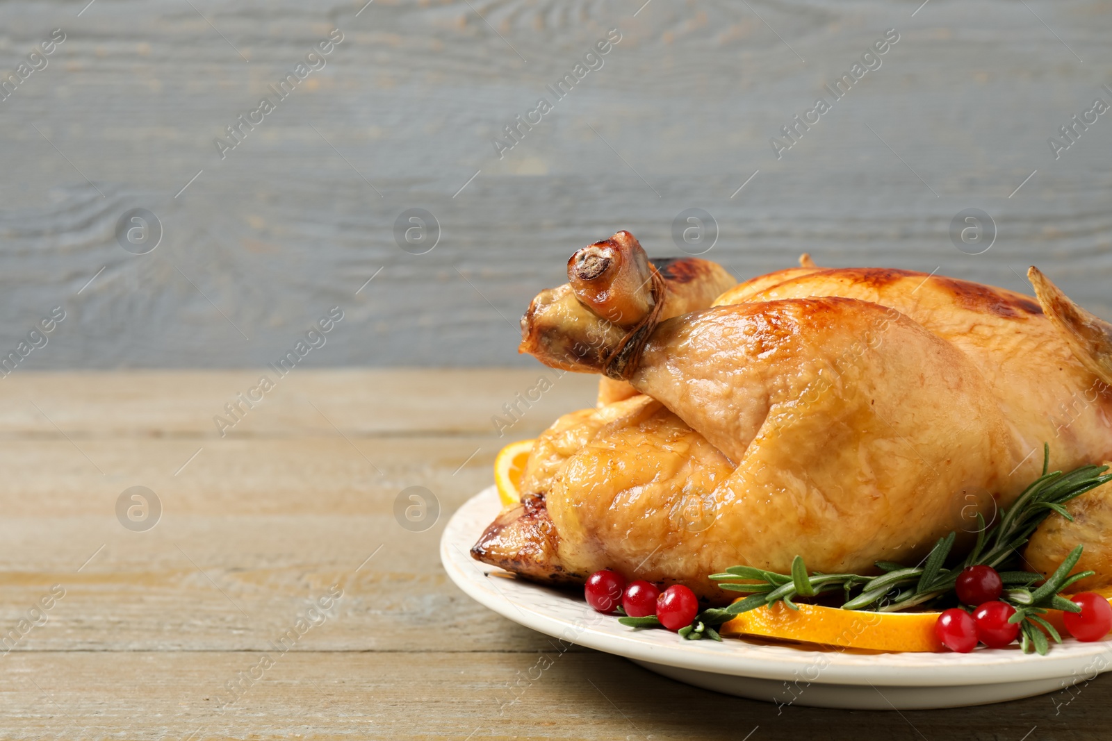 Photo of Delicious cooked turkey served with rosemary, oranges and cranberries on wooden table, space for text. Thanksgiving Day celebration