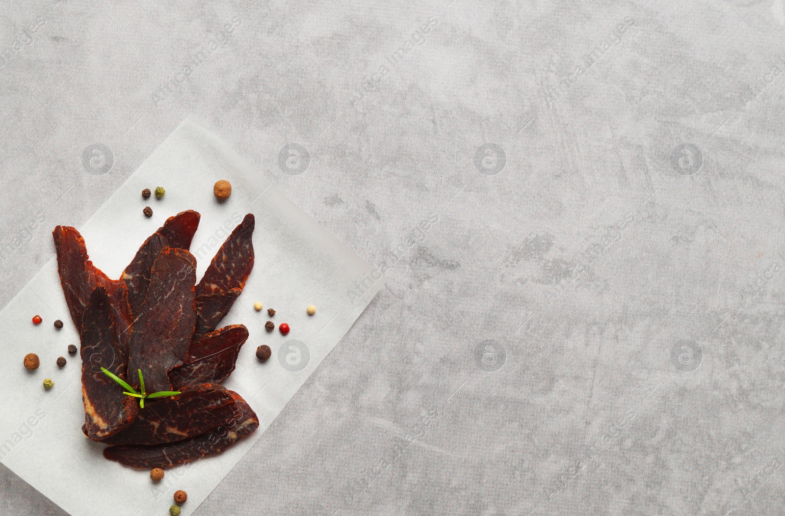 Photo of Pieces of delicious beef jerky and spices on light grey table, top view. Space for text