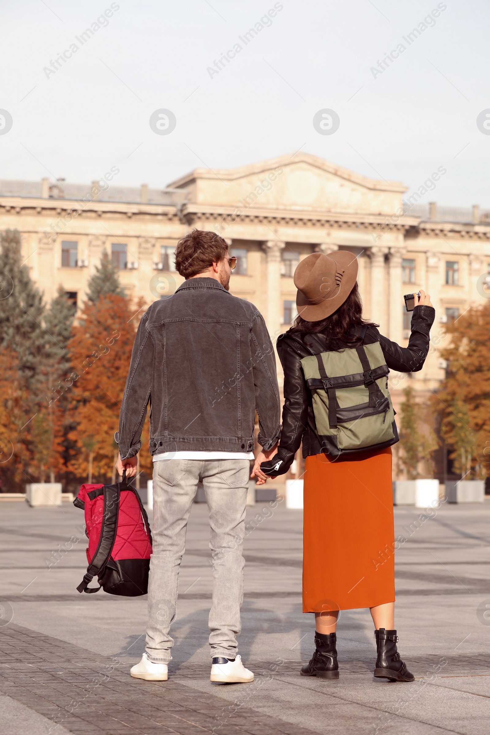 Photo of Couple of travelers with backpacks on city street, back view