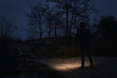 Photo of Man with flashlight walking near river in evening