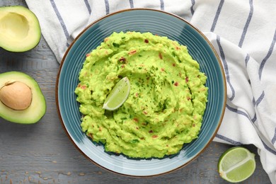 Photo of Delicious guacamole with lime and fresh avocado on grey wooden table, flat lay