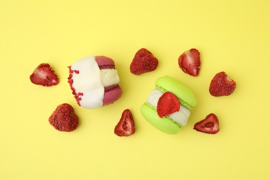 Photo of Delicious macarons and dry strawberries on yellow background, flat lay