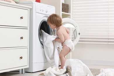 Little girl pulling baby clothes out of washing machine indoors