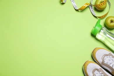 Photo of Sport shoes, apples, water and measuring tape on green background, flat lay. Space for text