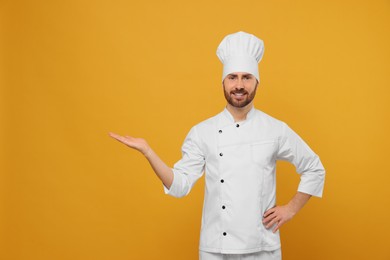 Photo of Smiling mature chef showing something on orange background, space for text