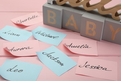 Photo of Cubes with word Baby and paper stickers with different names on pink wooden table. Choosing baby's name