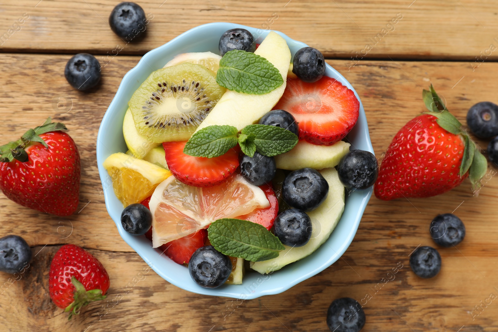 Photo of Tasty fruit salad in bowl and ingredients on wooden table, flat lay